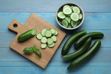 Fresh ripe cucumbers and basil on light blue wooden table, flat lay