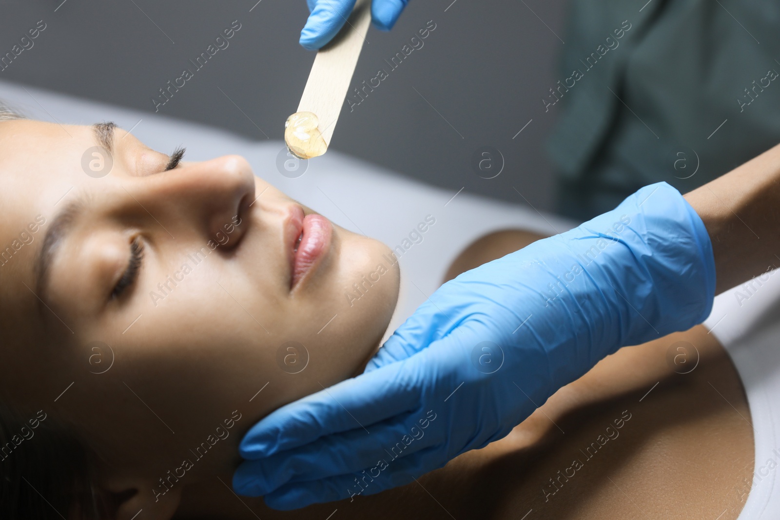 Photo of Young woman undergoing hair removal procedure on face with sugaring paste in salon