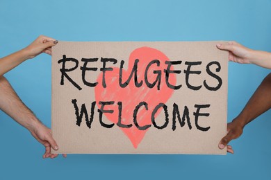 Image of People holding sign with phrase WELCOME REFUGEES on light blue background, closeup