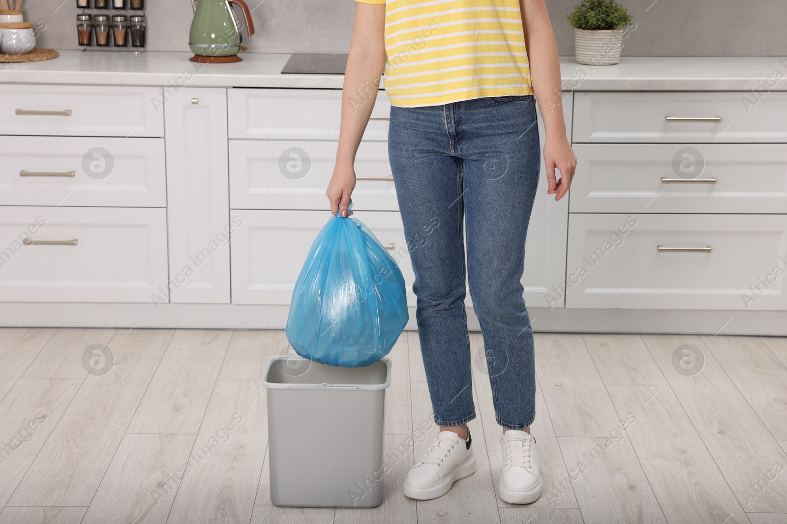 Photo of Woman taking garbage bag out of trash bin in kitchen, closeup