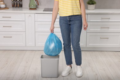 Photo of Woman taking garbage bag out of trash bin in kitchen, closeup