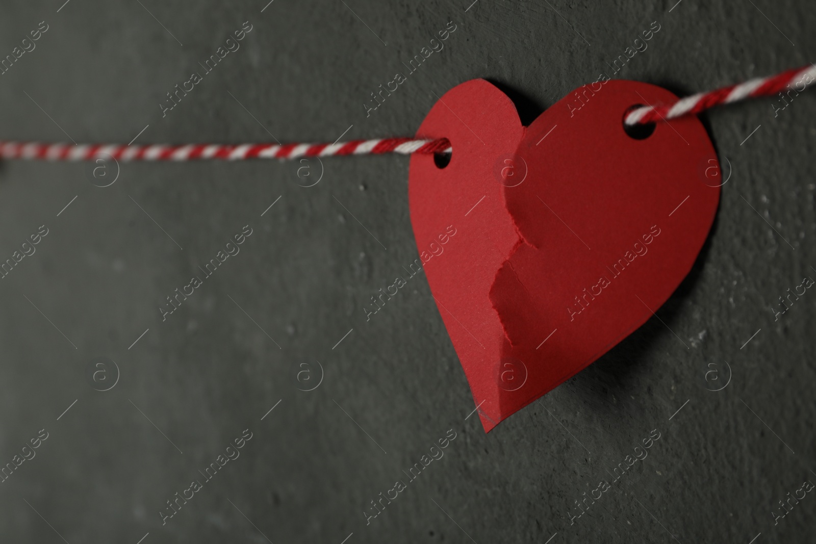 Photo of Broken red paper heart on rope near black wall, space for text. Relationship problems concept