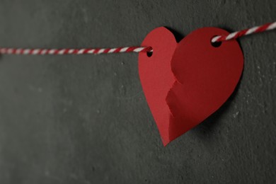 Photo of Broken red paper heart on rope near black wall, space for text. Relationship problems concept