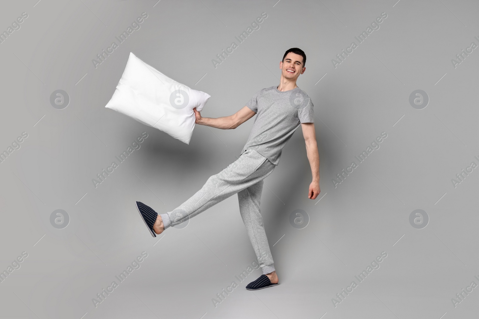 Photo of Happy man in pyjama holding pillow on grey background