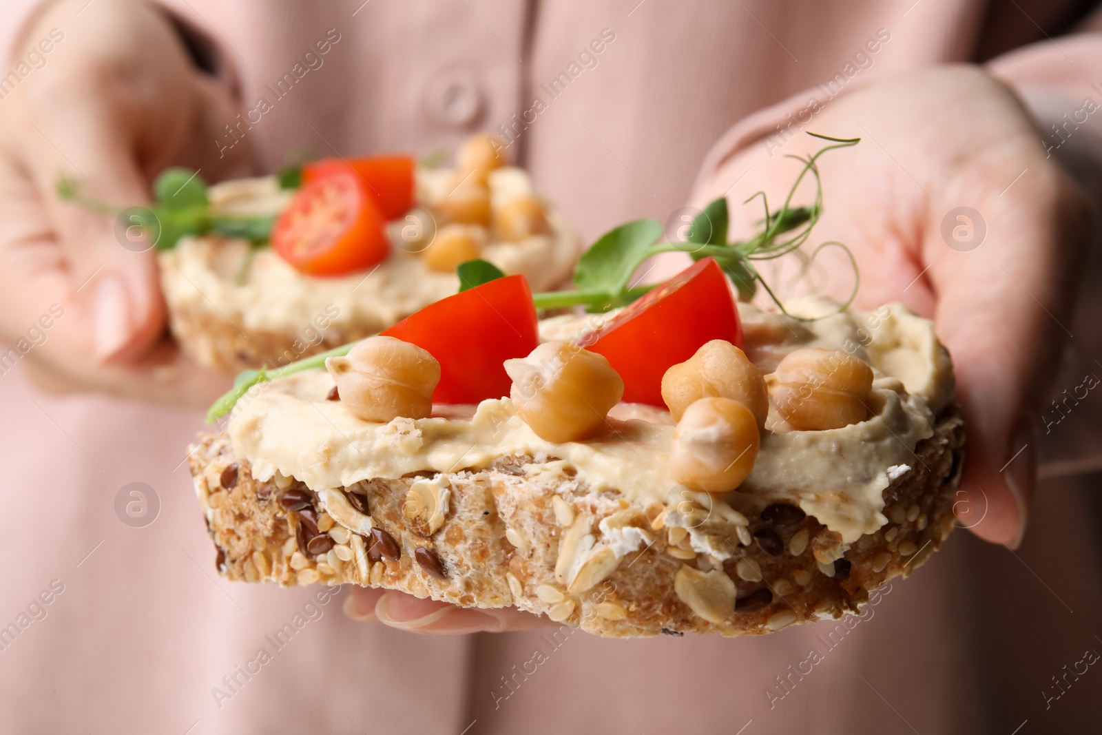 Photo of Woman holding delicious sandwiches with hummus , tomato slices and chickpeas , closeup