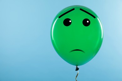 Image of Green balloon with sad face on light blue background. Space for text