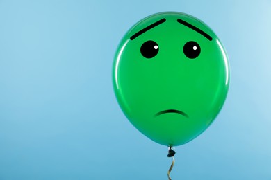 Green balloon with sad face on light blue background. Space for text