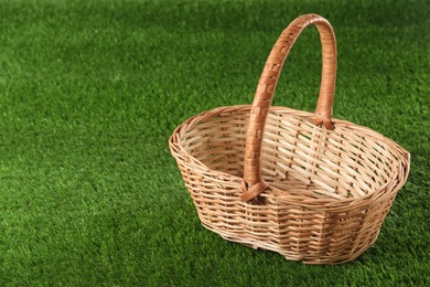 Empty wicker basket on green lawn, space for text. Easter item