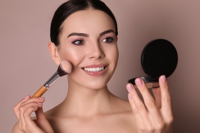 Photo of Beautiful young woman applying face powder with brush on dusty rose background, closeup