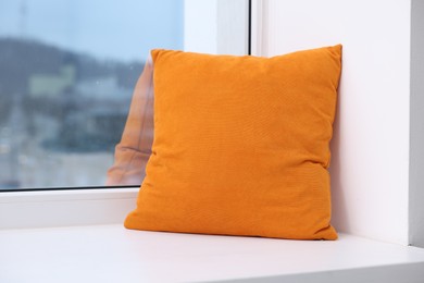 Photo of Orange soft pillow on window sill indoors