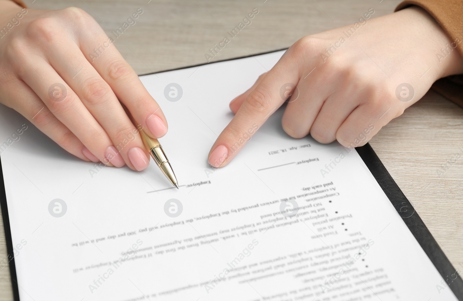 Photo of Woman signing document at wooden table, closeup