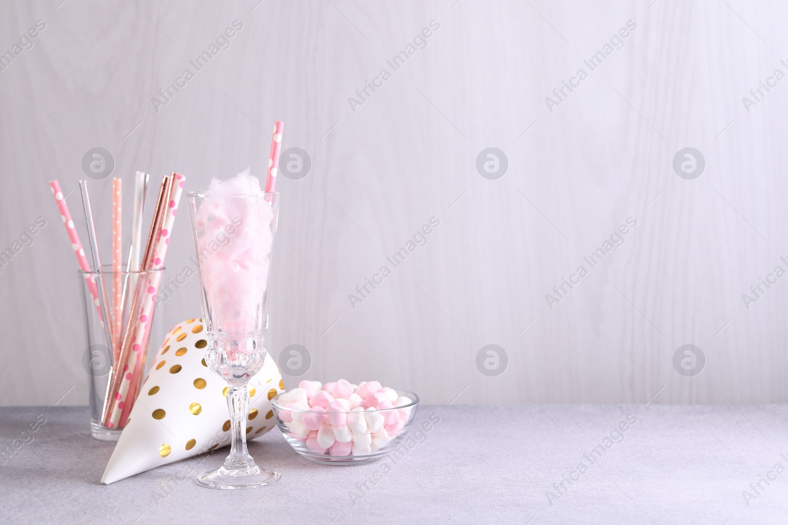 Photo of Tasty cotton candy cocktail in glass, festive decor and marshmallows on gray table against light wooden wall, space for text