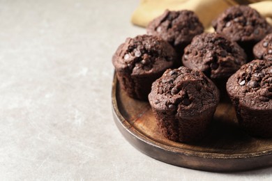 Photo of Board with delicious chocolate muffins on light table, closeup. Space for text