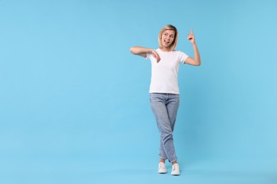 Happy woman pointing on light blue background, space for text