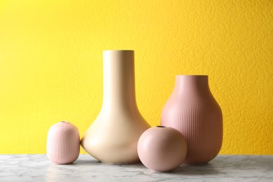 Stylish ceramic vases on white marble table against yellow background