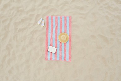 Striped beach towel, book, straw hat and flip flops on sand, aerial view