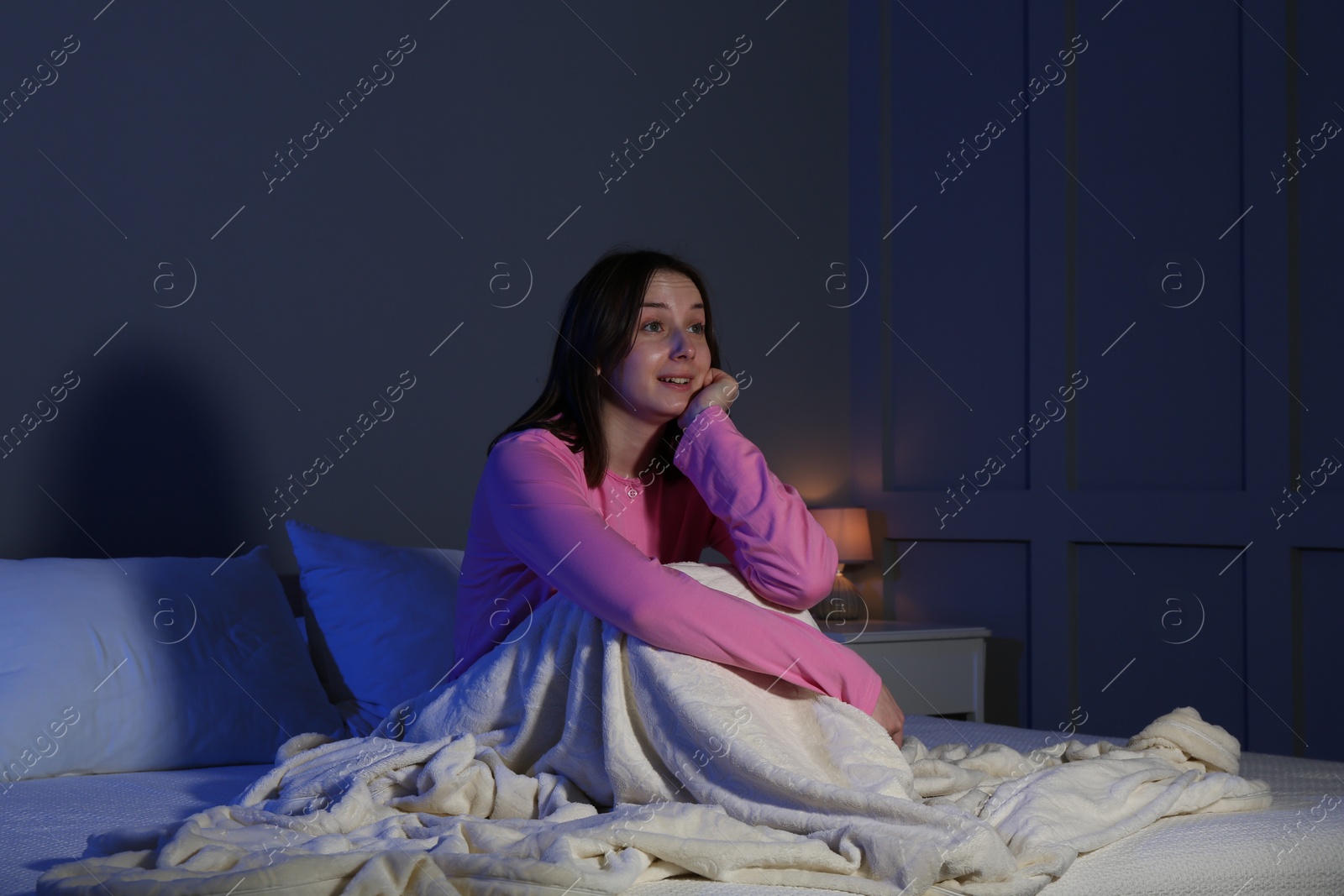 Photo of Young woman watching TV on bed at night