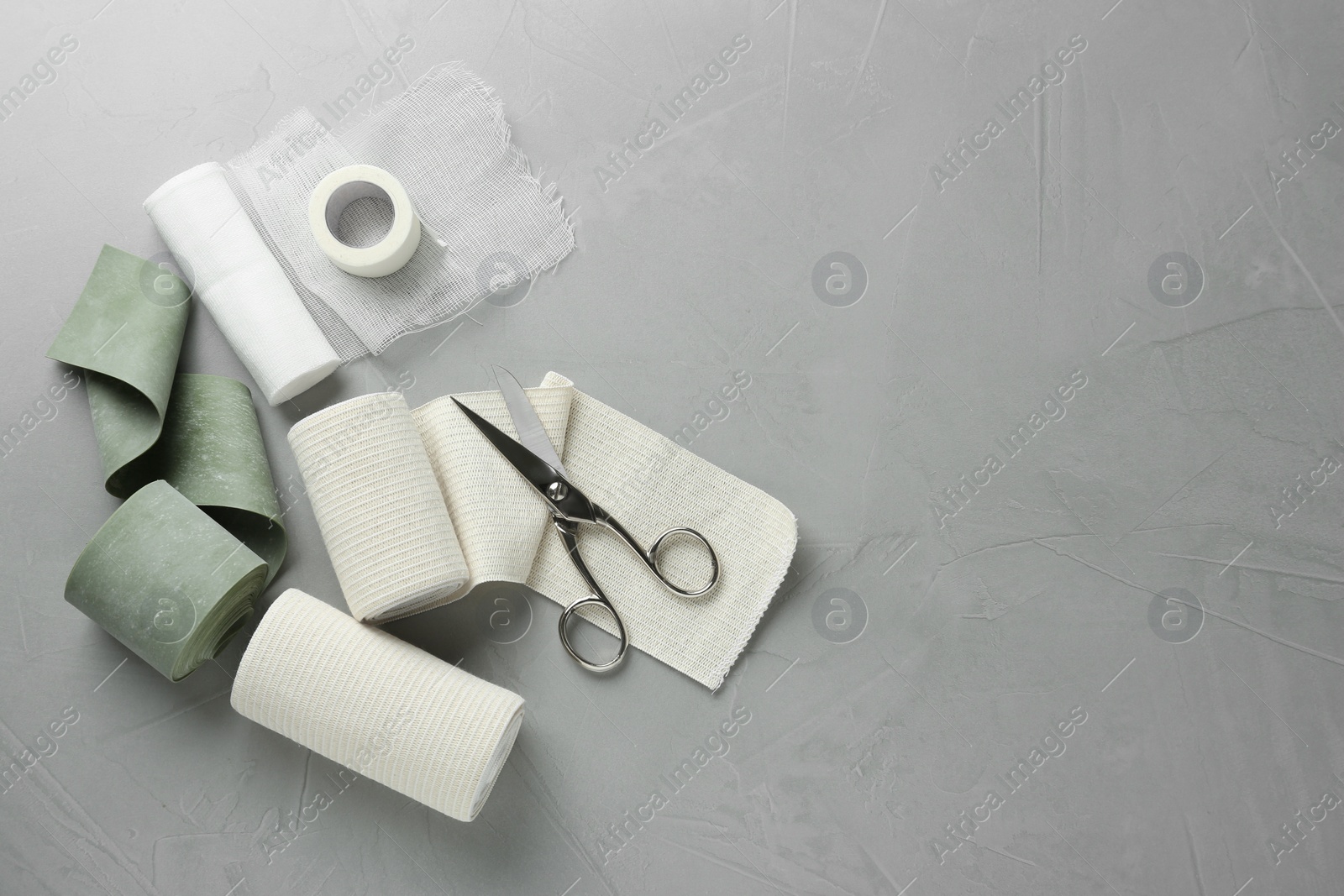 Photo of Medical bandage rolls, sticking plaster and scissors on grey table, flat lay. Space for text