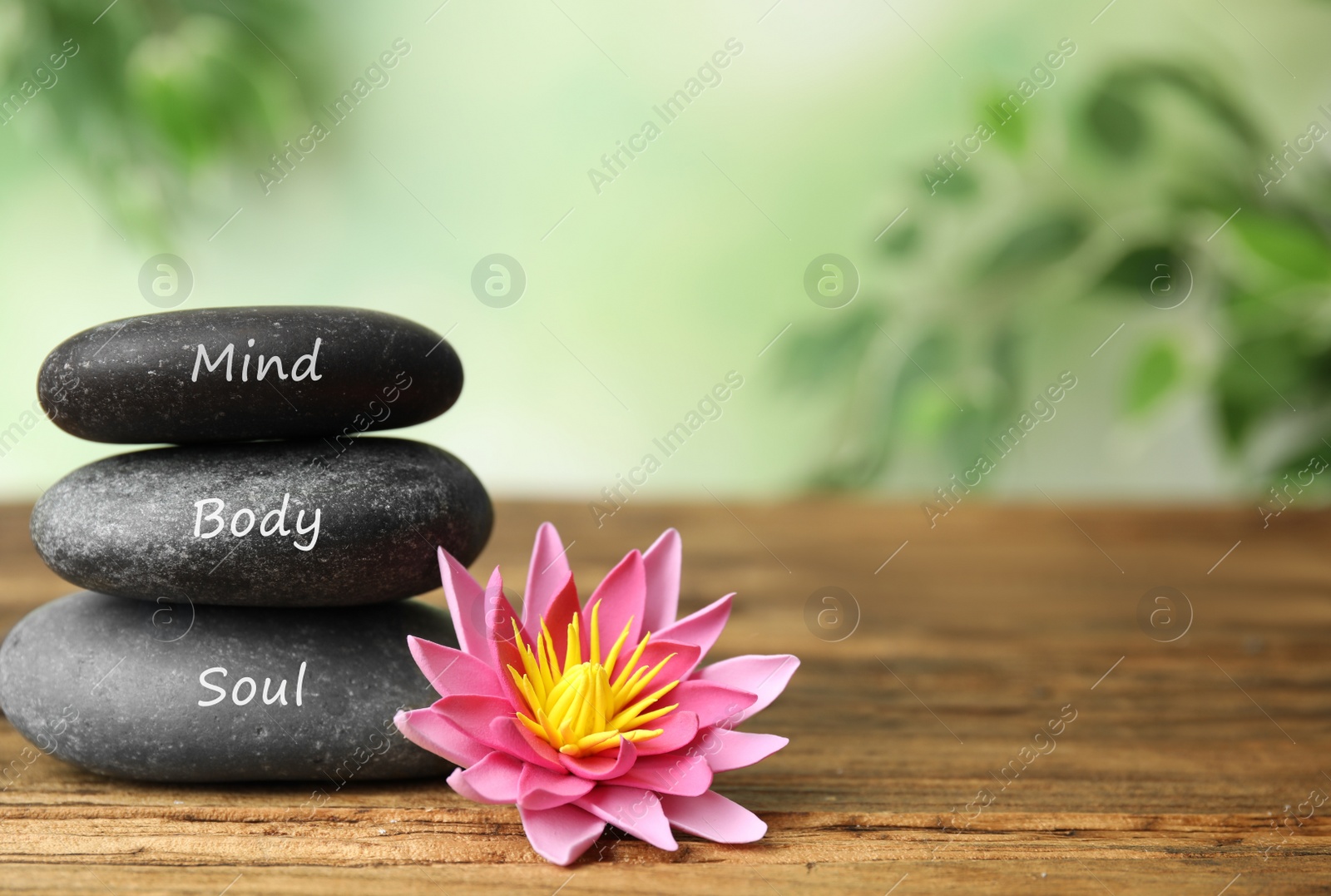 Photo of Stones with words Mind, Body, Soul and lotus flower on wooden table, space for text. Zen lifestyle