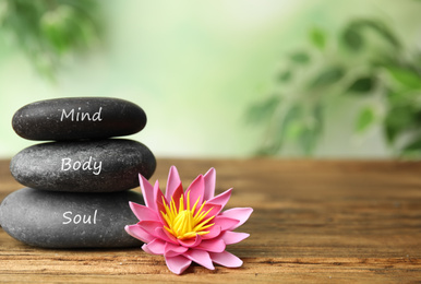 Photo of Stones with words Mind, Body, Soul and lotus flower on wooden table, space for text. Zen lifestyle