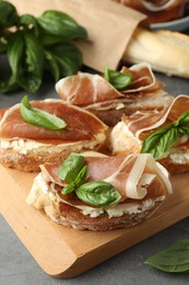 Photo of Tasty sandwiches with cured ham and basil on grey table, closeup