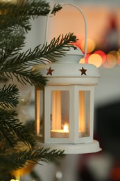 Christmas lantern with burning candle on fir tree indoors, closeup