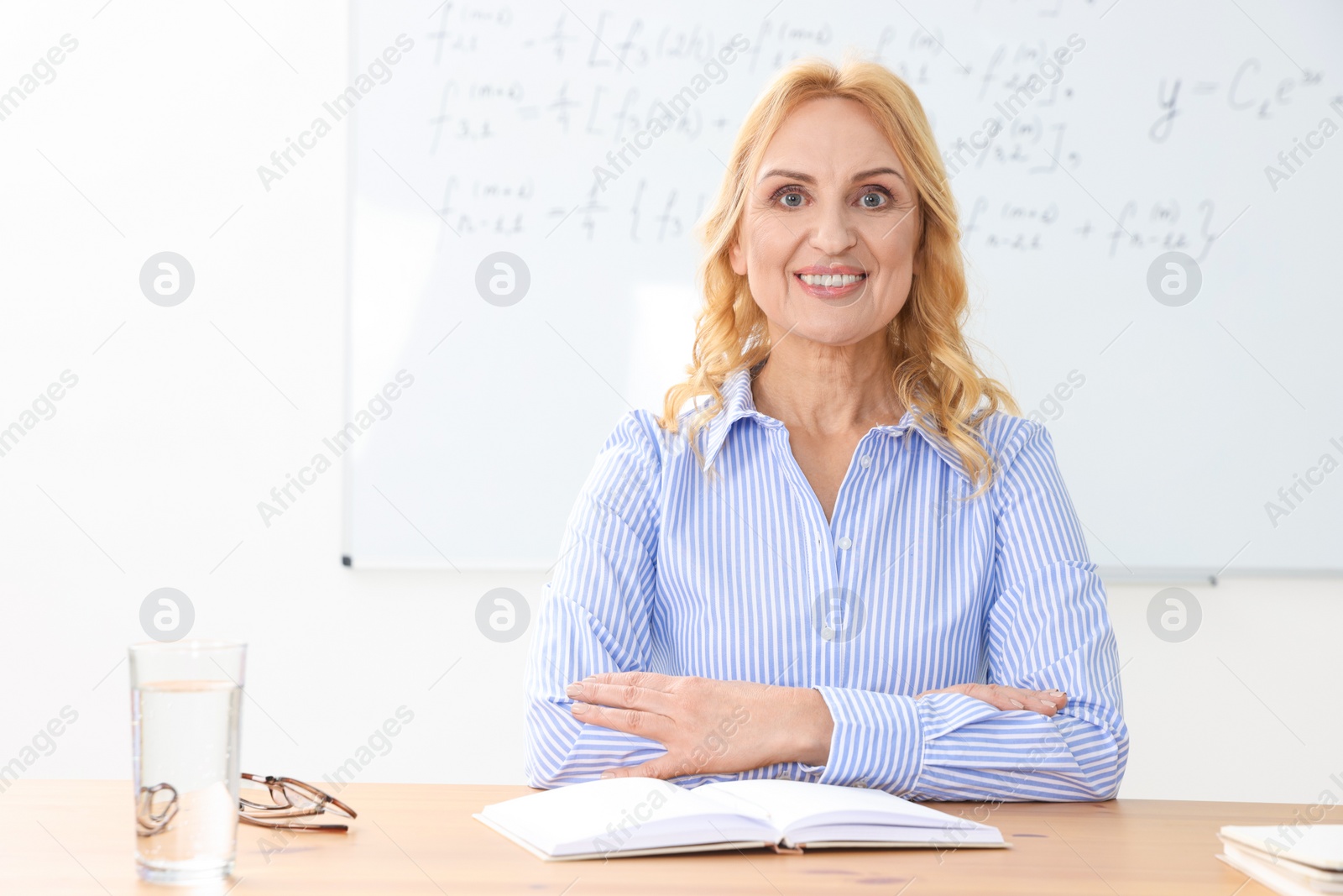 Photo of Happy teacher with book sitting at desk in classroom