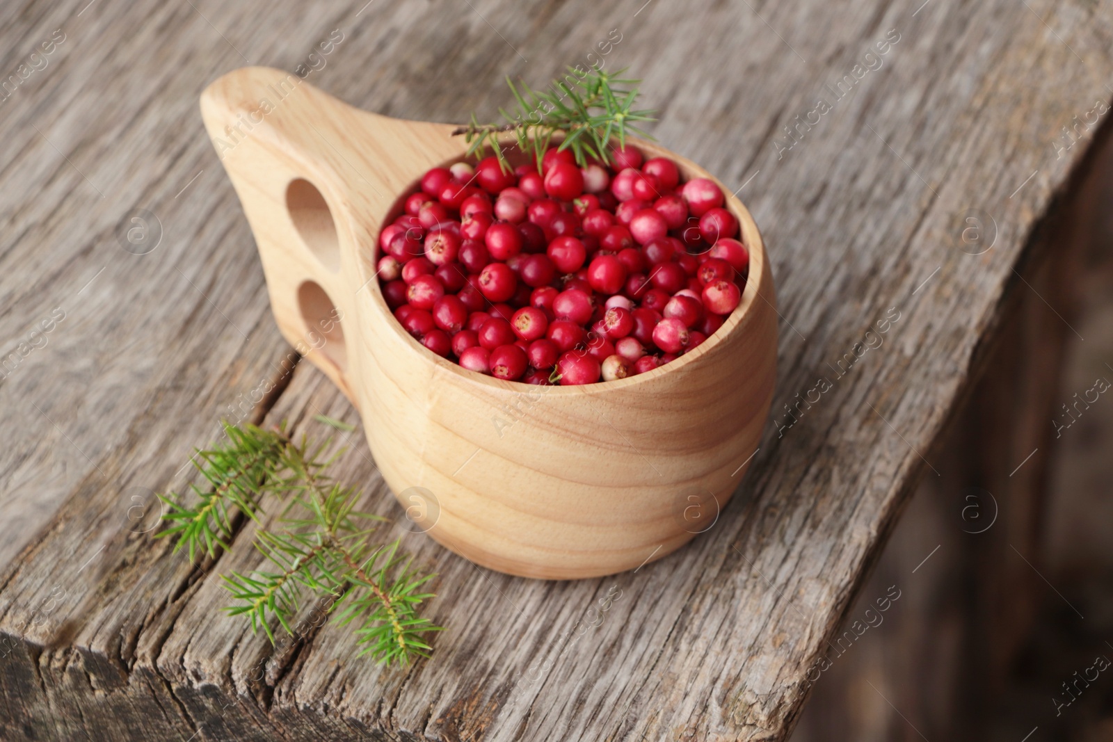 Photo of Cup with tasty ripe lingonberries and spruce twigs on wooden surface