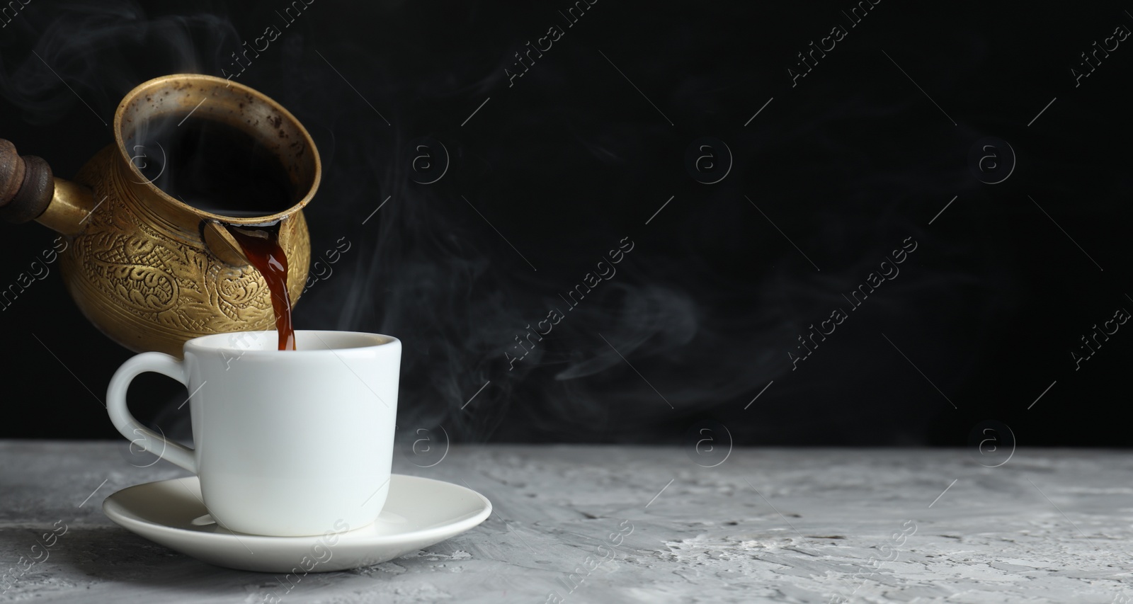 Image of Turkish coffee. Pouring freshly brewed beverage from cezve into cup on grey table. Banner design with space for text