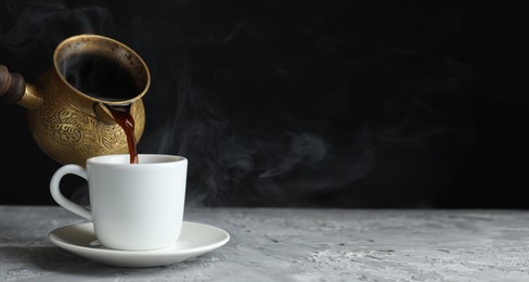 Image of Turkish coffee. Pouring freshly brewed beverage from cezve into cup on grey table. Banner design with space for text