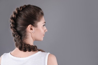 Woman with braided hair on grey background, back view. Space for text