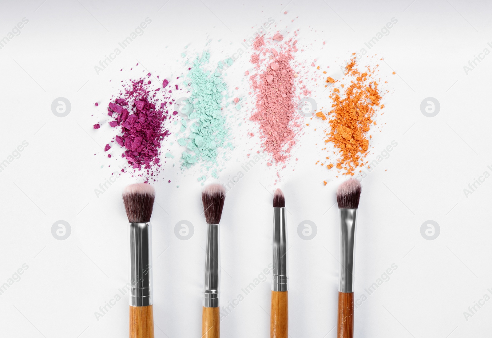 Photo of Makeup brushes and scattered eye shadows on white background, flat lay