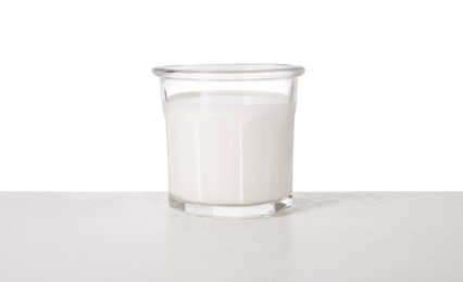 Photo of Glass of tasty milk on light table against white background