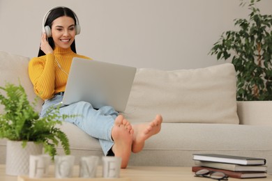 Woman with laptop and headphones sitting on sofa at home