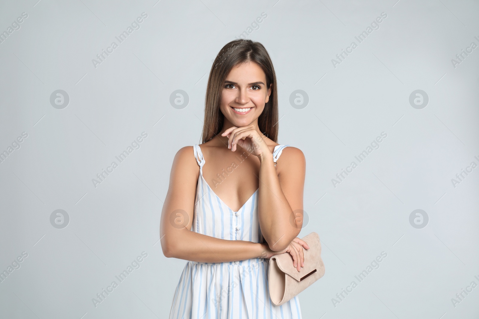 Photo of Young woman wearing stylish dress with elegant clutch on light grey background