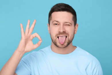 Photo of Happy man showing his tongue and OK gesture on light blue background