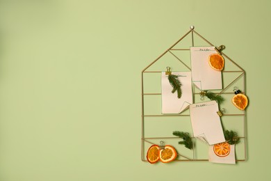 Photo of Christmas decor made of dry orange slices, notes and fir tree branches on light green wall. Space for text