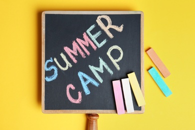 Photo of Words SUMMER CAMP written with colorful chalk on small blackboard, top view