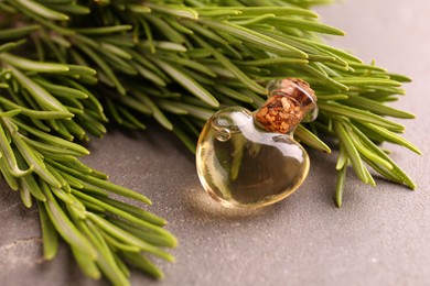 Photo of Essential oil in bottle and rosemary on grey table, closeup