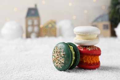 Different decorated Christmas macarons on table with artificial snow, space for text