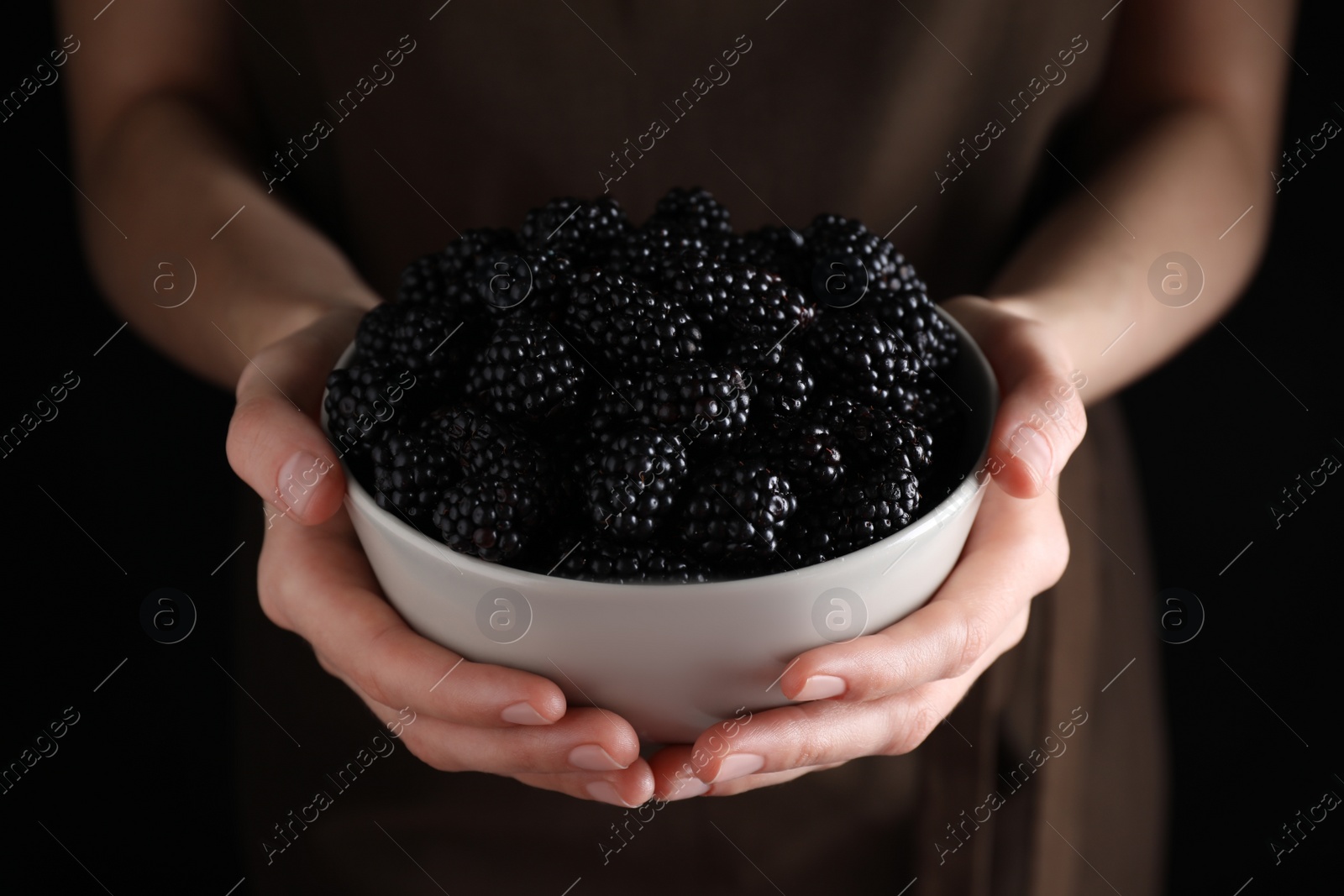 Photo of Woman with bowl of fresh blackberries against dark background, closeup