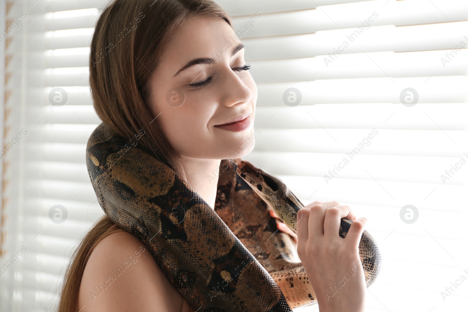 Photo of Young woman with boa constrictor at home. Exotic pet