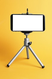 Photo of Modern tripod with smartphone on yellow background