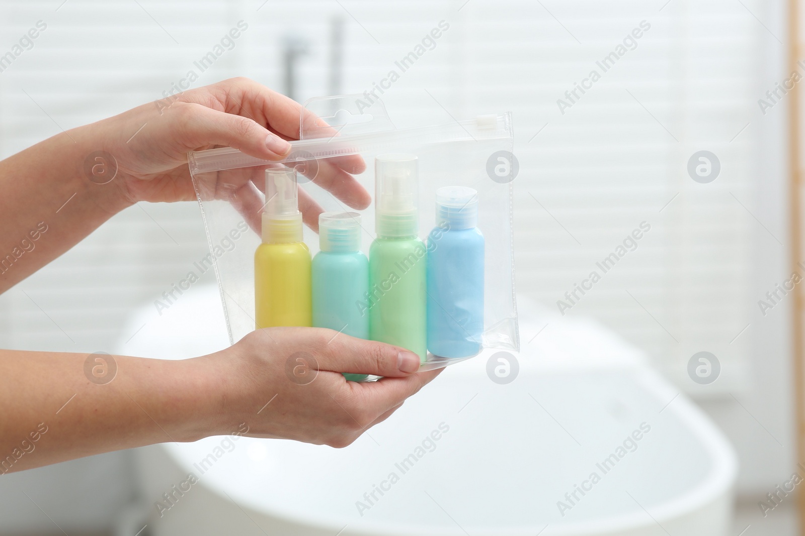 Photo of Woman with plastic bag of cosmetic travel kit in bathroom, closeup and space for text. Bath accessories