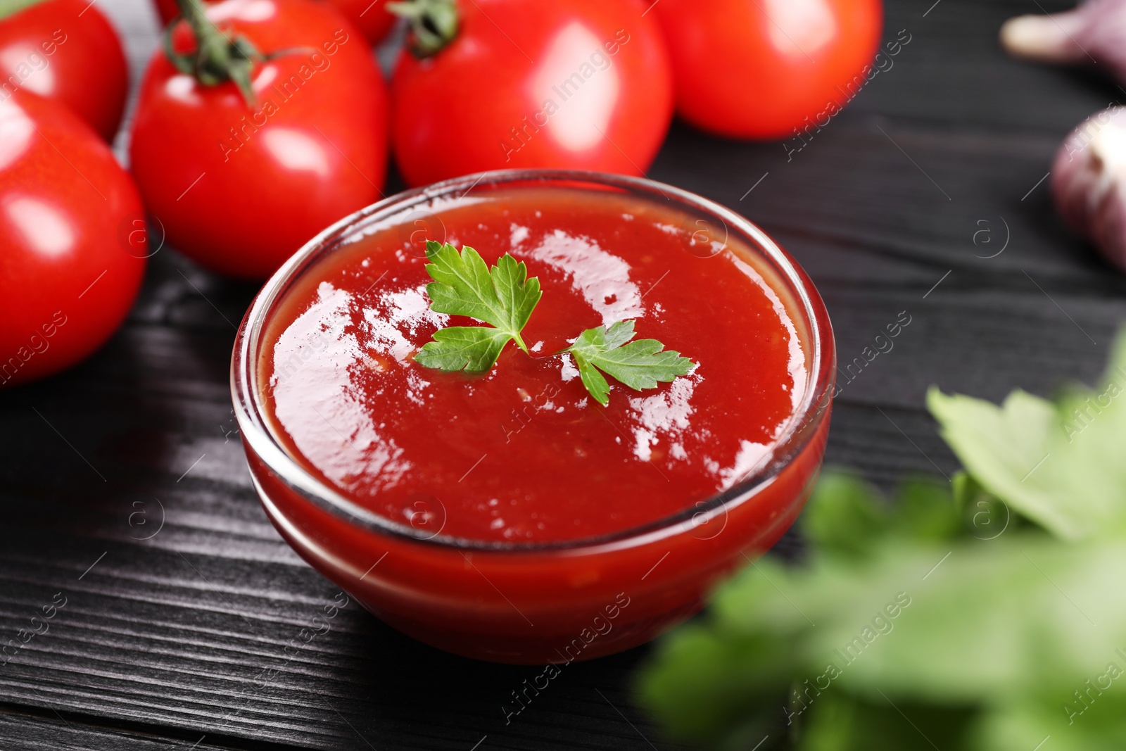 Photo of Delicious ketchup in bowl and tomatoes on black wooden table, closeup. Tomato sauce