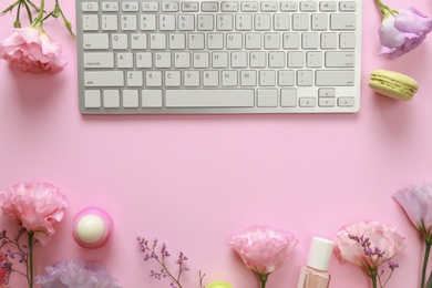 Flat lay composition with keyboard and flowers on pink background. Beauty blogger's workplace