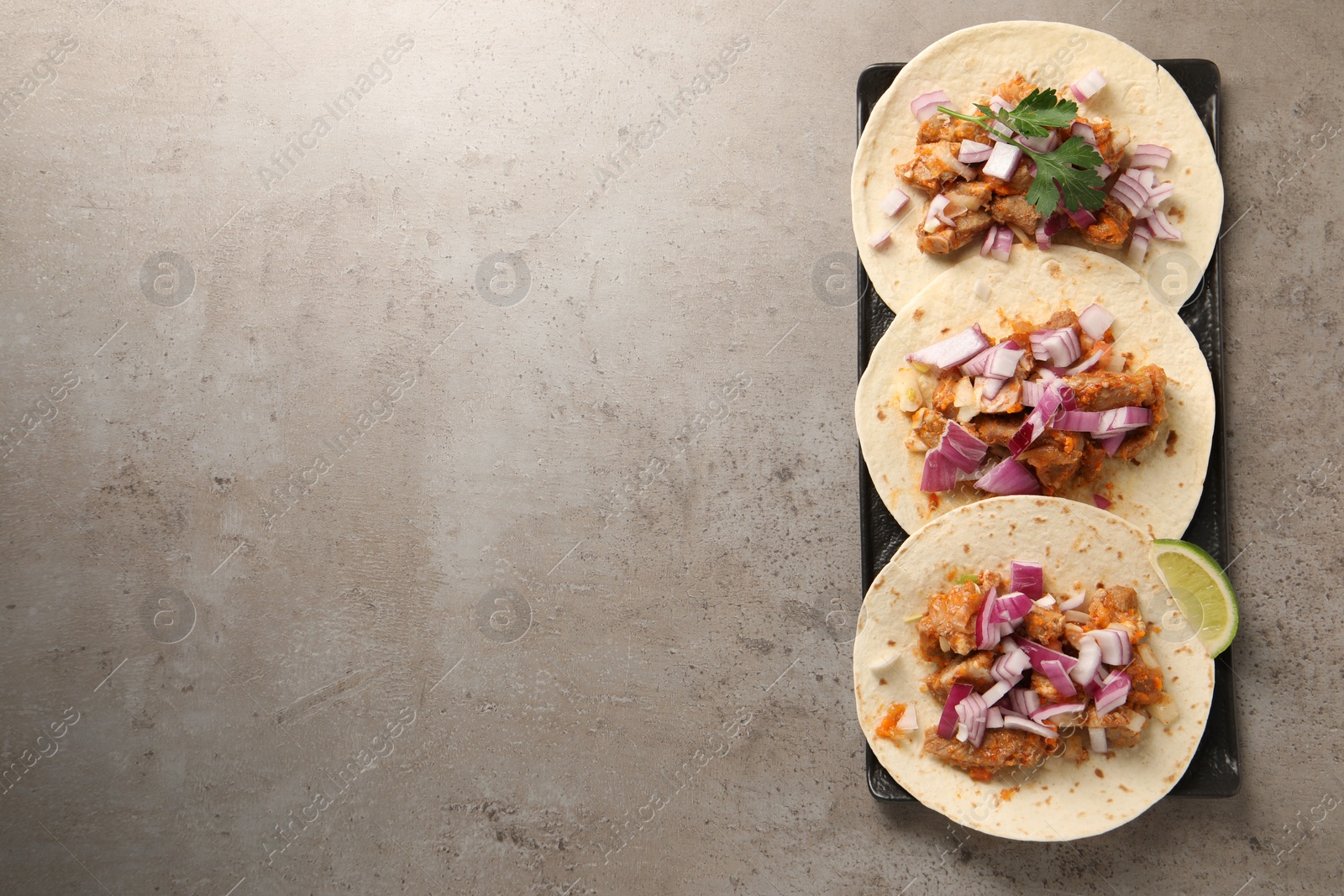 Photo of Delicious tacos with vegetables, meat and lime on grey textured table, top view. Space for text