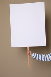 Woman holding blank sign on beige background, closeup. Space for design