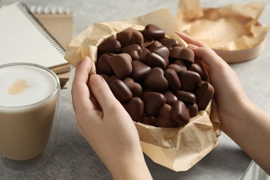 Photo of Woman holding box with heart shaped chocolate candies at light grey table, closeup