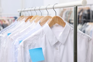 Dry-cleaning service. Many different clothes in plastic bags hanging on rack indoors, closeup